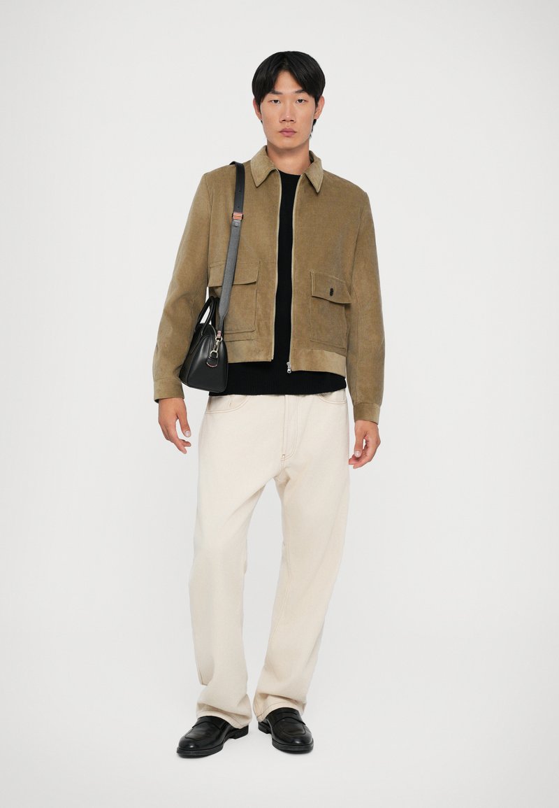 Brun corduroy jakke med lynlås, sort sweater under, creme farvede vide bukser og sorte sko. Lille skuldertaske med rem.