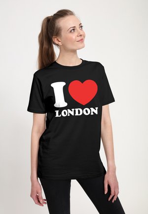 Young woman with a ponytail wearing a black T-shirt that says "I ❤️ LONDON," standing with one hand relaxed and looking to the side.