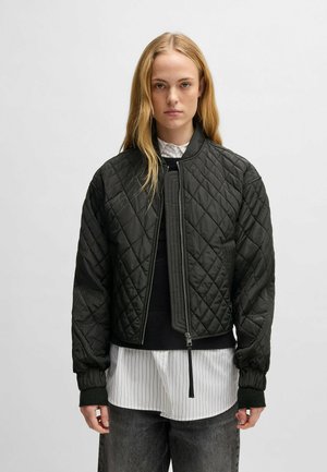 Quilted black bomber jacket with ribbed knit cuffs and hem, featuring a front zipper and side pockets, layered over a striped shirt.
