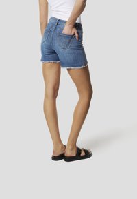 Short en jean avec ourlet effiloché, couleur bleue, poches arrière et coupe taille mi-haute. Associé à des sandales noires à enfiler.