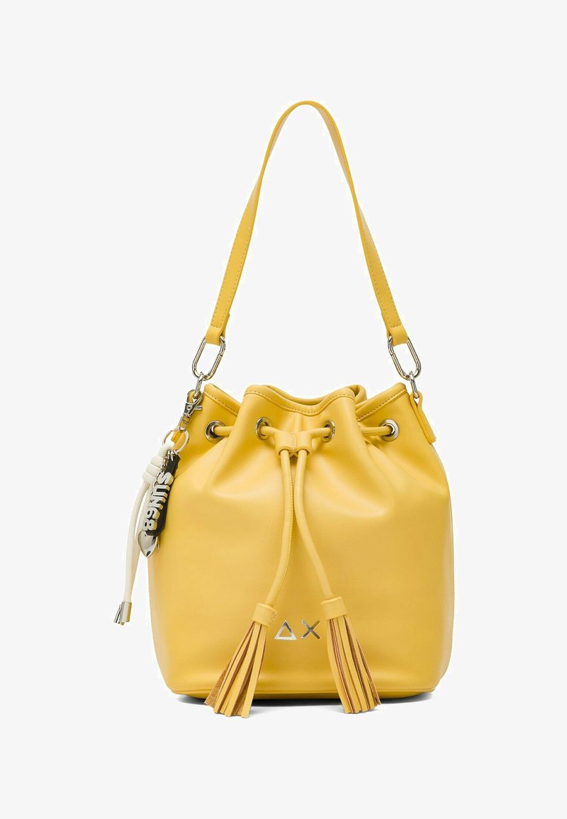 Borsa a secchiello in pelle gialla con coulisse a nappe, tracolla singola, occhielli metallici e accessorio portachiavi nero e bianco.