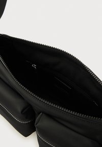 Μαύρη υφασμάτινη τσάντα με φερμουάρ και εσωτερική τσέπη, με ομαλή υφή και διακριτικές λεπτομέρειες ραφής κατά μήκος των ραφών.