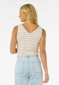 Top sans manches en V, avec un motif rayé beige et crème, associé à un jean bleu clair taille haute avec des poches arrière.