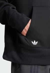 Černá mikina s kapucí, přední kapsou, manžetami na rukávech a bílým logem Adidas na dolním levém rohu. Vyrobena z měkkého, texturovaného materiálu.