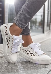 Weiße Sneaker mit durchbrochener Blumenstruktur, flacher Sohle und weißen Schnürsenkeln. Texturierte Oberfläche und goldene Ösen betonen den Gesamteindruck.