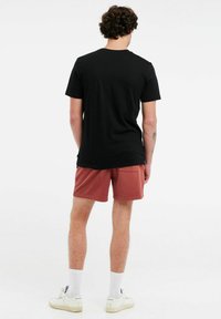 Maglietta nera in cotone abbinata a pantaloni corti corallo, vista da dietro, con un design minimalista e sneakers bianche con calzini di colore chiaro.