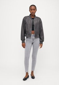 Grå faux skinn bomberjakke med ribbestrikkede mansjetter og nederkant, båret over en svart crop top, sammen med grå smale jeans og svarte flate sko.
