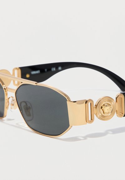 Μαύρα γυαλιά ηλίου με φακούς και χρυστά γεωμετρικά πλαίσια, και χρυσό έμβλημα κεφαλής Μέδουσας στα βραχίονα των γυαλιών.