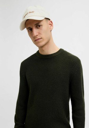 Green knitted sweater with a textured pattern, crew neckline, and long sleeves. The model wears a light-colored cap with embroidered text.