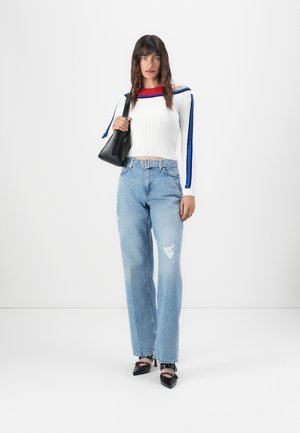 White ribbed sweater with red neckline and blue stripes, paired with light blue wide-leg distressed jeans and black pointed-toe shoes.