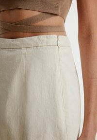 Beige Baumwollrock mit tailliertem Bund, der mit einem verdeckten Reißverschluss und klaren Linien versehen ist. Strick-Crop-Top in Braun mit gekreuzten Trägern.