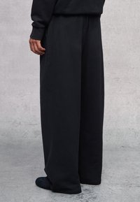 Pantalones de pierna ancha negros en una suave mezcla de algodón con una cinturilla elástica. Presenta un diseño minimalista y una textura lisa.