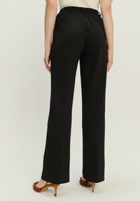 Schwarze, hochgeschlossene Hose mit lockerer Passform, ausgestattet mit einem elastischen Bund und zwei Gesäßtaschen. Glattes Material mit einem sauberen Finish.