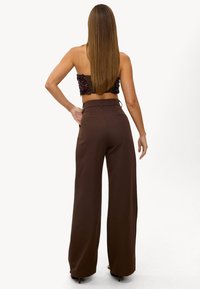 Pantalon marron taille haute à jambes larges avec une texture lisse et un design minimaliste, associé à un crop top à sequins, vu de dos.