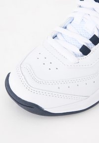 Fehér sneaker bőr felső résszel, texturált hálós nyelvvel és sötét navy kiegészítőkkel. Perforációkkal és kontrasztos varrással rendelkezik a szellőzés érdekében.
