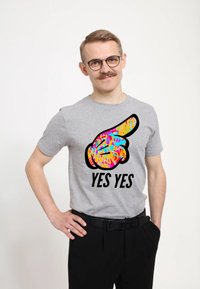Šedé tričko s krátkým rukávem, které má barevnou grafiku ukazující ruku a text "ANO ANO" v černé barvě. Hladký materiál z bavlněné směsi.