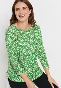 Grünes Top mit floralem Muster, dreiviertelärmlig, runder Ausschnitt und lockerer Passform. Hergestellt aus weichem, leichtem Stoff.