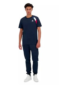 Abbigliamento sportivo blu navy composto da una t-shirt a maniche corte con un design multicolore sulle spalle e pantaloni della tuta coordinati. Tessuto uniforme e vestibilità.