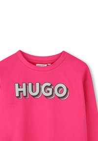 Roze katoenen T-shirt met een ronde hals, voorzien van het woord "HUGO" in vetgedrukte, zilveren 3D-lettertype aan de voorkant.