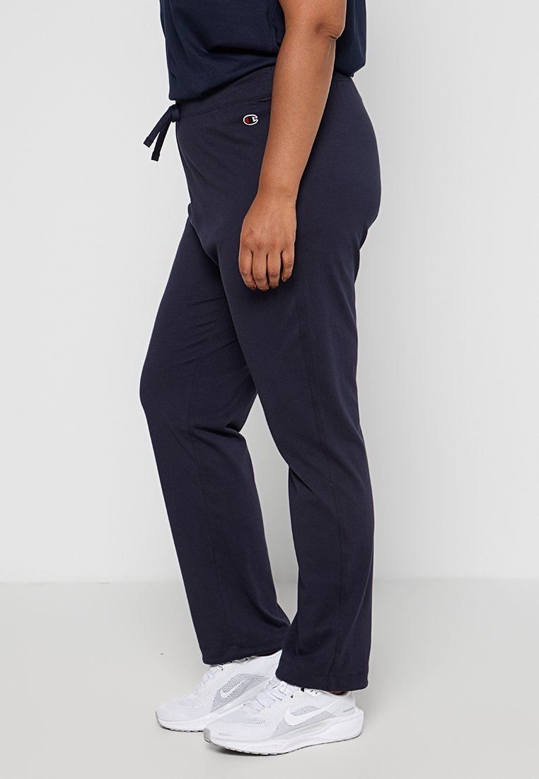 Pantalons de jogging en navy, doux et extensibles, avec une taille à cordon et un logo, associés à des chaussures de sport blanches. Texture lisse et coupe décontractée.