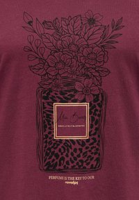 Bordeauxrode T-shirt met een zwart bloemmotief in een pot met een luipaardprintpatroon, gouden accenten en de tekst "Miss Beauty Absolutely Blooming."