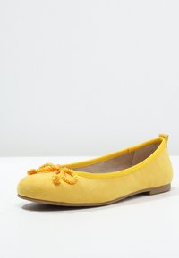 Žluté semišové baletní byty s kulatou špičkou, které mají vpředu pletený provázek jako ozdobu a hladkou plochou podrážku.