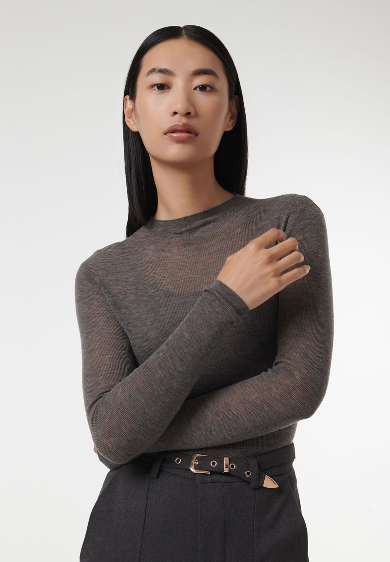 Grijze, ribbelige top met lange mouwen en een aansluitende silhouette, met een hoge halslijn en zachte textuur. Gecombineerd met hooglopende marineblauwe broeken en een riem.