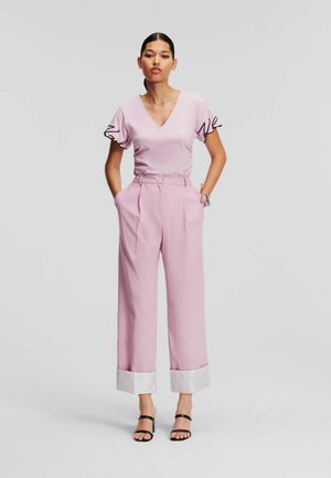 Pale pink top with ruffled black-edged sleeves, paired with high-waisted pale pink trousers featuring white striped cuffs. Black sandals.