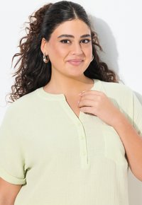 Maglietta verde chiaro a maniche corte con scollo henley bottonato, tessuto texturizzato e taschino sul petto. Presenta una vestibilità comoda.
