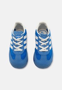 Chaussures de sport bleues en suède et tissu, avec des rayures blanches et des lacets blancs. Bout rond, col rembourré et semelle en caoutchouc.