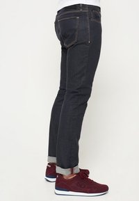 Tummansiniset hoikentavat farkut, joissa on kontrastisaumat, viiden taskun malli ja käännetyt lahkeet. Yhdistetty viininpunaisiin tennareihin.