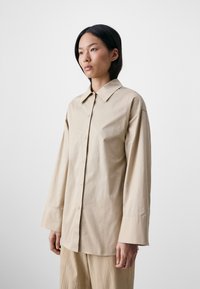 Pikad varrukad ja nööbid in beige puuvillane särk, klassikalise kraega, mugava lõikega ja kerge tekstuuriga. Ühtlane värv, ei mingeid mustreid.