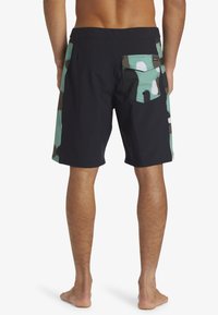 Zwarte zwembroek voor heren met een teal en bruin camouflagemotief aan de zijkanten. Voorzien van een achterzak en een ontwerp tot halverwege de dij.