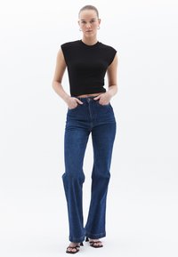 Top corto a coste nero con maniche a sbuffo, abbinato a jeans a campana blu in denim a vita alta e sandali neri con tacco; stile minimalista.