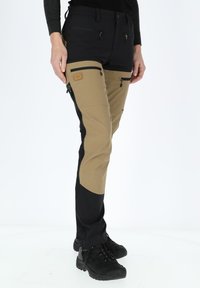 Trekkingbroeken met een zwart en kaki ontwerp, voorzien van ritszakken en versterkte naden. Gemaakt van duurzaam, flexibel materiaal.