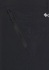 Mustat vaellushousut, joissa on vetoketjullinen sivutasku, sileä pinta, vahvistetut saumat ja logo vyötärönauhassa.