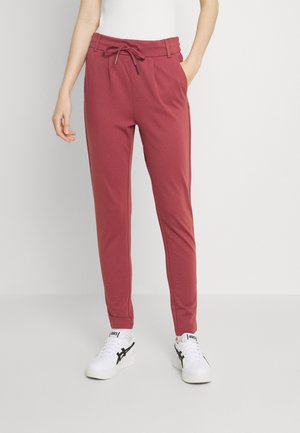 Pantalons de jogging bordeaux avec une taille élastique, un cordon de serrage, des poches latérales et une coupe fuselée, assortis de chaussures de sport blanches.