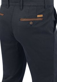 Marineblauwe katoenen broek met gestikte details, tan lederen accenten op de zakken en een knoopsluiting, ontworpen voor veelzijdig gebruik.