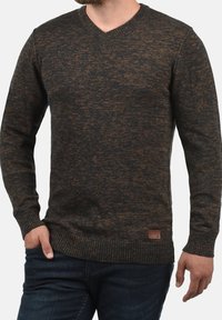 Pull en V marron foncé avec un motif de tricot texturé, doté d'un ourlet et de poignets côtelés, ainsi qu'une petite étiquette en cuir sur le côté.