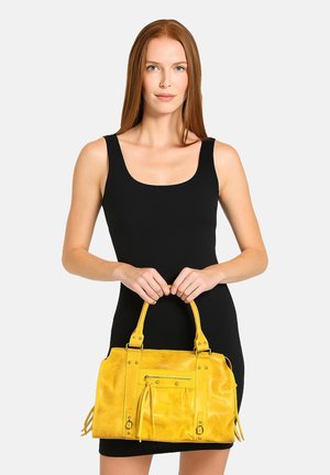 Borsa a mano gialla in pelle con doppio manico, tasca frontale con zip e dettagli con frange. Texture liscia con accessori in metallo chiodato.