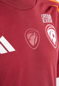 Maillot de sport rouge avec des rayures blanches Adidas, logos brodés sur la poitrine et un col haut. Texture de tissu douce.