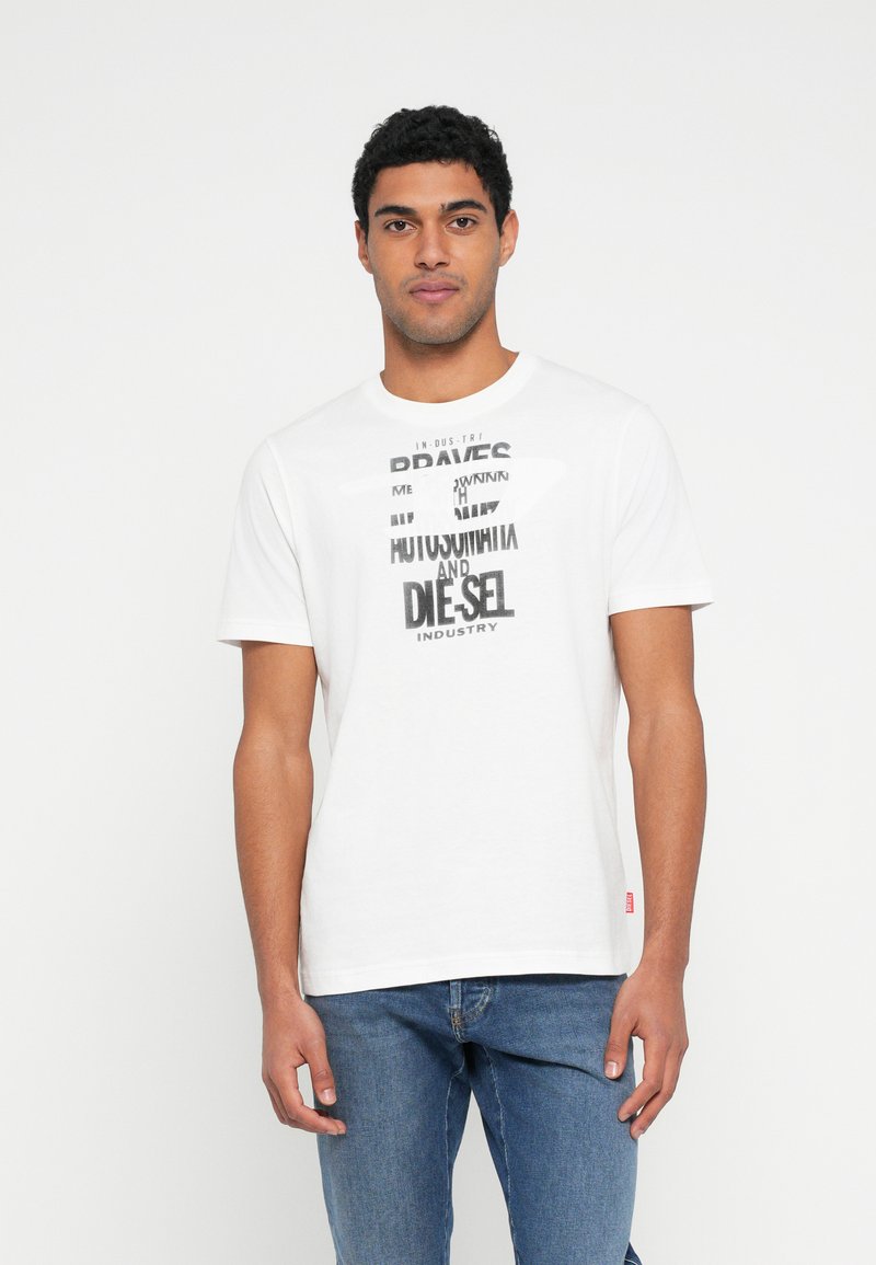 Tricou alb din bumbac cu text grafic negru în fonturi variate, cu mâneci scurte și guler rotund, asortat cu blugi albaștri.