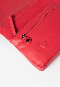 Clutch in pelle rossa con due scomparti con zip, texture liscia, bordi arrotondati e dettagli in metallo nero. Dettagli trapuntati visibili.