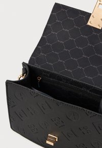 Čierna kabelka cez telo s embosovanými vzormi, zlatými kovaniami a vnútorným vreckom na zips. Podšívka z čierneho materiálu s logom.