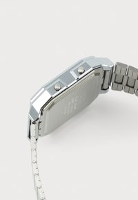Montre-bracelet en métal argenté avec un boîtier rectangulaire, deux boutons et un bracelet à maillons. L'arrière est lisse avec des détails gravés.