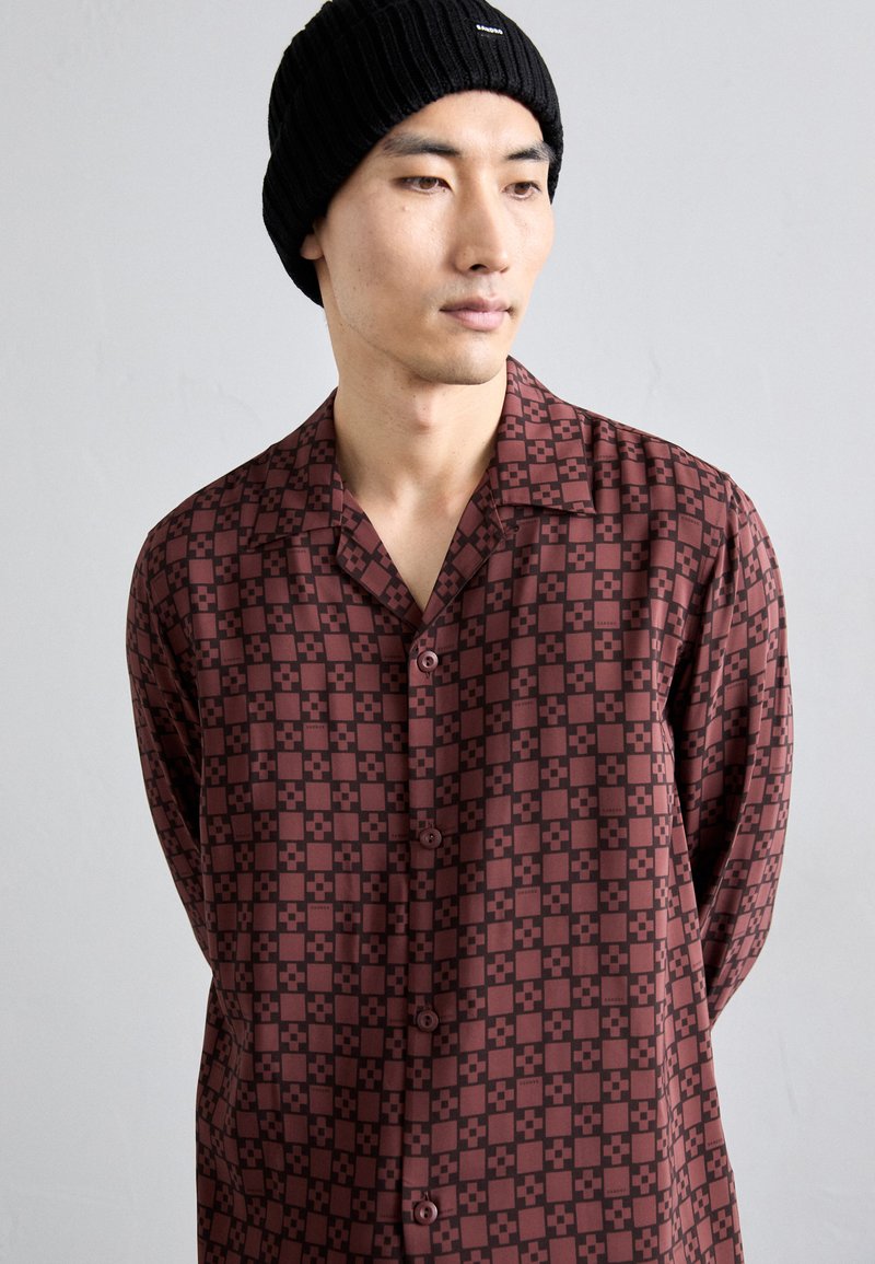 Camicia button-up bordeaux con un motivo geometrico in tonalità più scure, dotata di colletto a scollatura e vestibilità rilassata. Tessuto morbido.