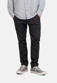 Pantalones negros de corte slim, hechos de una tela suave, con un corte clásico y bolsillos laterales. Combinados con zapatillas de lona gris.