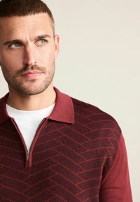 Burgundská polokošeľa na zips s textúrovaným diamantovým vzorom na tele a jednofarebným golierom, ktorý má bielu vnútornú vrstvu.