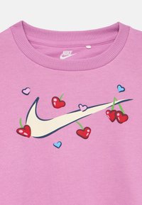 Ροζ φούτερ Nike με μεγάλο λευκό λογότυπο swoosh διακοσμημένο με κεράσια σε σχήμα κόκκινων καρδιών και μικρές μπλε και ροζ καρδιές.