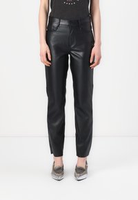 Zwarte neplederen broek met een slim-fit ontwerp, voorzien van voorzakken en een soepele textuur, gecombineerd met schoenen met metallic details.